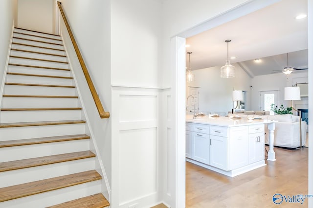 staircase featuring lofted ceiling, ceiling fan, and light wood-type flooring