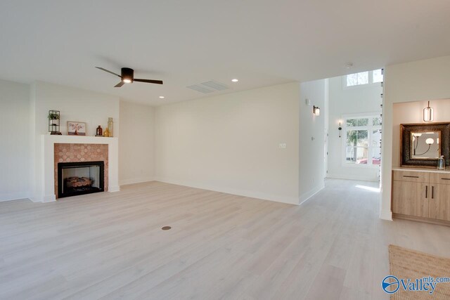 unfurnished living room with a tiled fireplace, ceiling fan, and light wood-type flooring