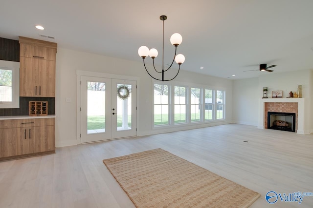 unfurnished living room with ceiling fan with notable chandelier, french doors, and light wood-type flooring