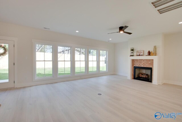 unfurnished living room featuring a tile fireplace, light hardwood / wood-style floors, and ceiling fan