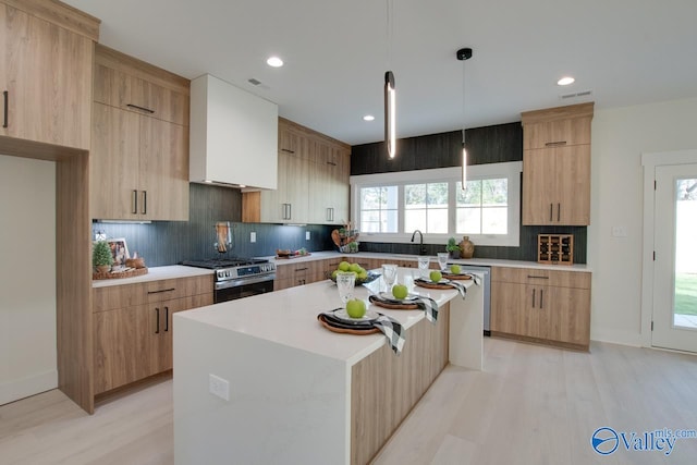 kitchen featuring backsplash, hanging light fixtures, a kitchen island, high end stove, and light hardwood / wood-style floors