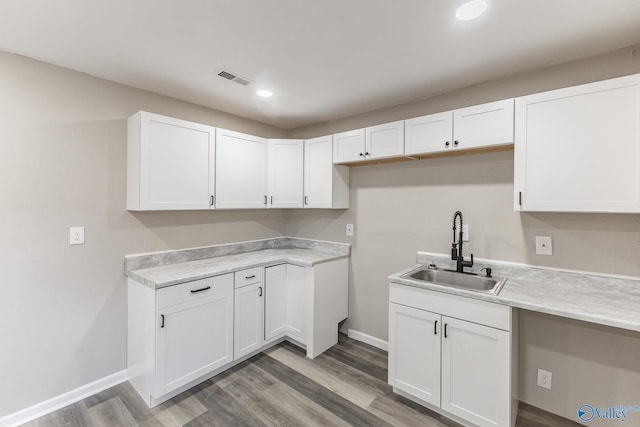 kitchen with light wood-type flooring, white cabinetry, light countertops, and a sink