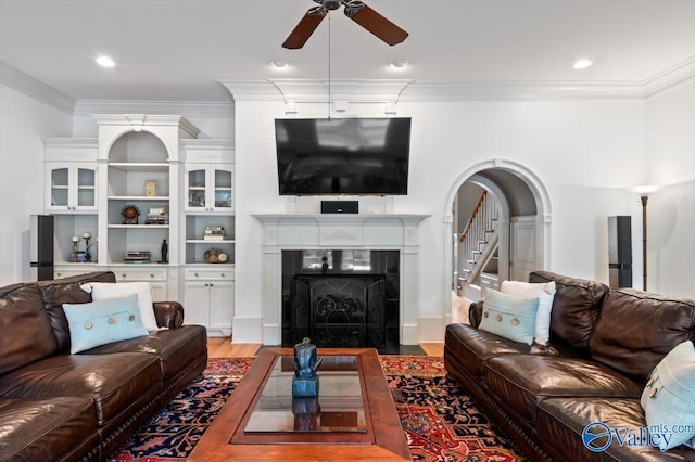 living room with ornamental molding, a fireplace, a ceiling fan, and light wood-type flooring