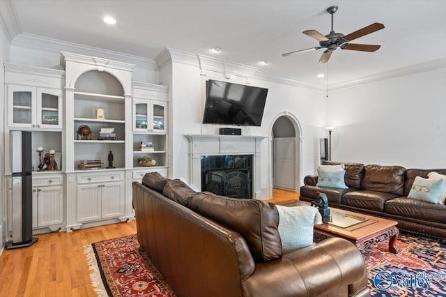 living room with recessed lighting, light wood finished floors, a ceiling fan, ornamental molding, and a fireplace