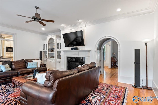 living room with arched walkways, light wood-style floors, ornamental molding, and ceiling fan