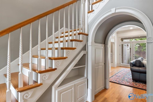 stairs with arched walkways, wood finished floors, and french doors