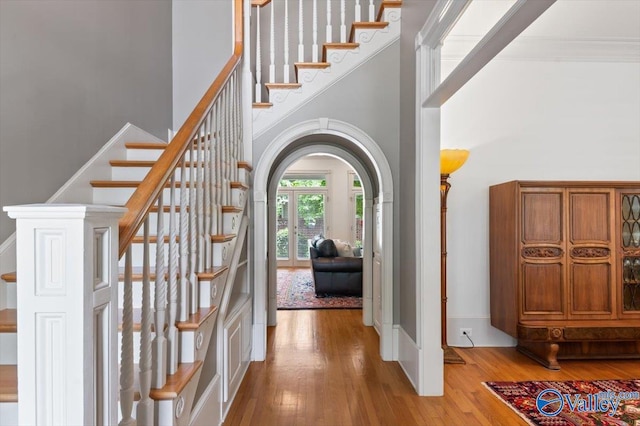 foyer entrance featuring wood-type flooring, arched walkways, a towering ceiling, and stairs