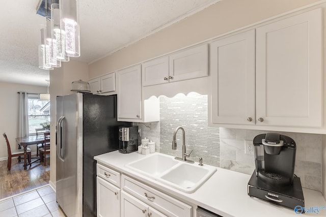 kitchen featuring light countertops, a sink, a textured ceiling, and stainless steel fridge with ice dispenser