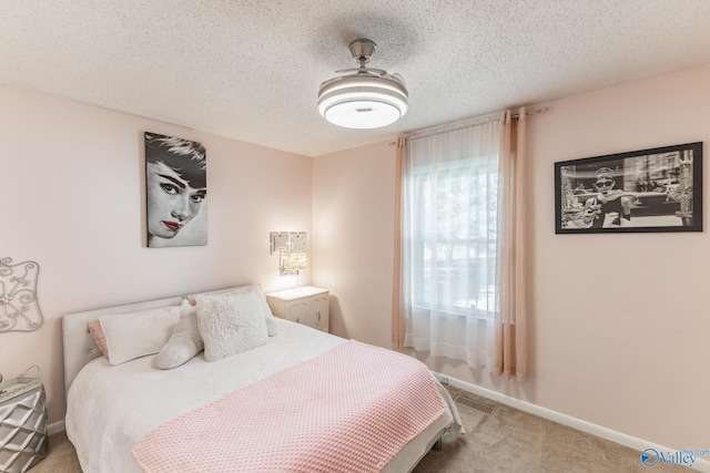 carpeted bedroom featuring a textured ceiling, visible vents, and baseboards