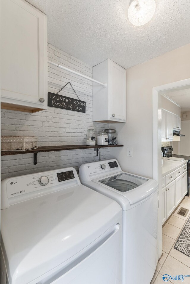 laundry room with a textured ceiling, light tile patterned flooring, visible vents, cabinet space, and washing machine and clothes dryer