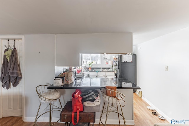 kitchen with a peninsula, light wood finished floors, a breakfast bar area, and freestanding refrigerator