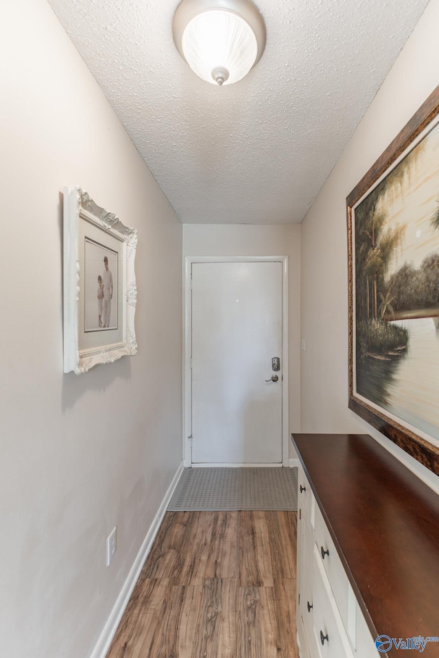 doorway to outside featuring a textured ceiling, wood finished floors, and baseboards