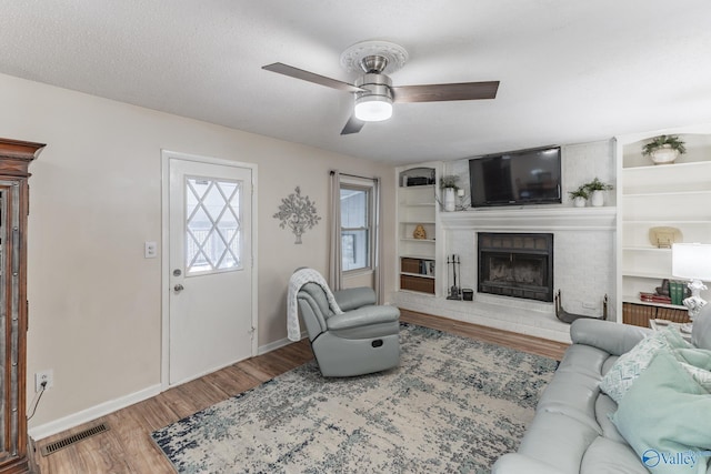 living room with baseboards, visible vents, wood finished floors, a textured ceiling, and a fireplace