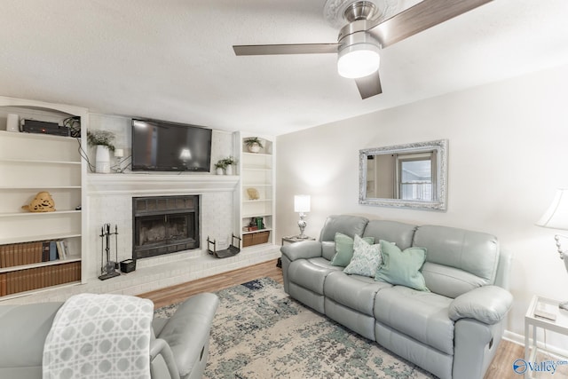 living area with a ceiling fan, a fireplace, a textured ceiling, and wood finished floors