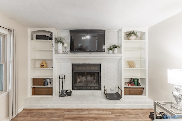 living room with a textured ceiling, a fireplace, wood finished floors, and built in features