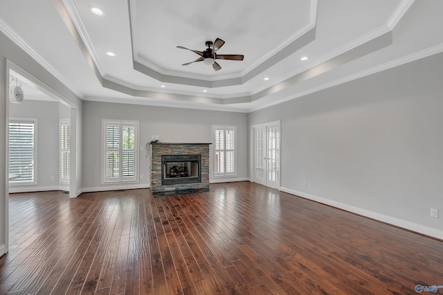 unfurnished living room with dark wood-type flooring, a stone fireplace, ornamental molding, and a tray ceiling