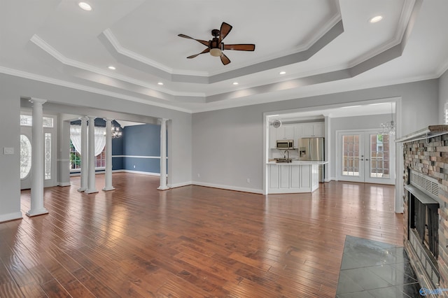 unfurnished living room with ceiling fan, a tray ceiling, ornamental molding, and decorative columns