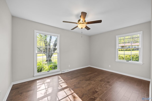 spare room featuring a ceiling fan, visible vents, a wealth of natural light, and dark wood-type flooring