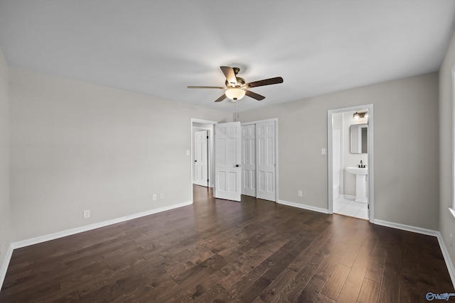 unfurnished bedroom featuring ensuite bathroom, baseboards, dark wood-type flooring, and a closet