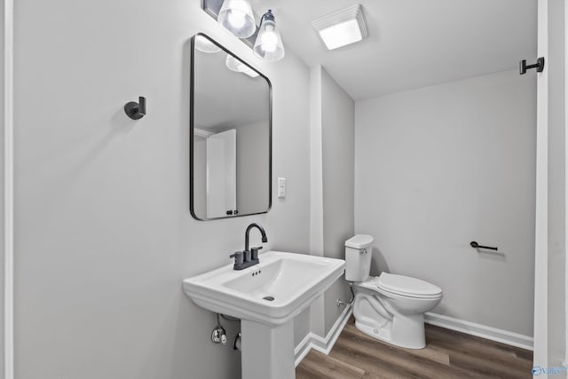 half bath featuring baseboards, wood finished floors, a sink, and toilet