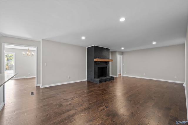 unfurnished living room with dark wood finished floors, baseboards, recessed lighting, a notable chandelier, and a fireplace