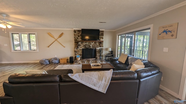 living room with crown molding, hardwood / wood-style flooring, a stone fireplace, and a wealth of natural light