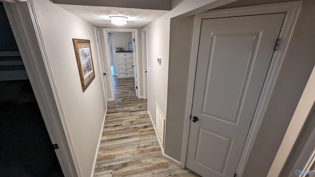 hall with a textured ceiling and light hardwood / wood-style flooring