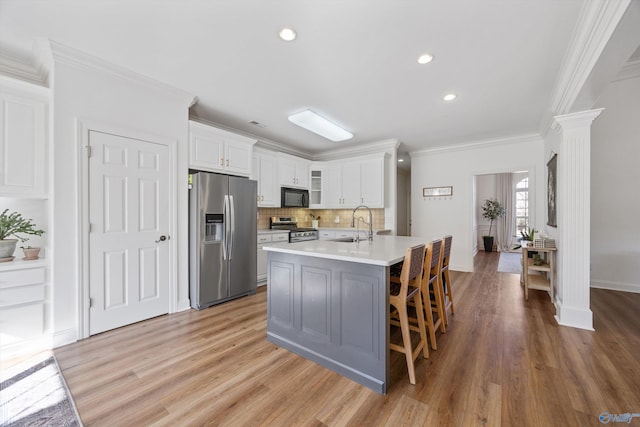 kitchen with light wood-style flooring, ornamental molding, stainless steel appliances, light countertops, and ornate columns