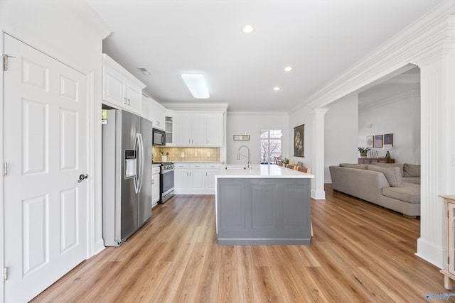 kitchen featuring open floor plan, light countertops, decorative backsplash, light wood-style flooring, and stainless steel appliances