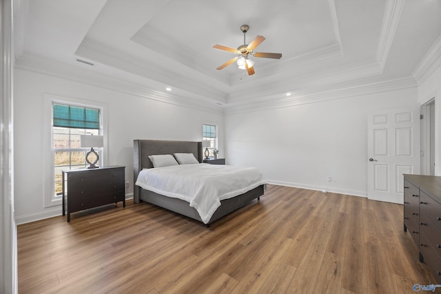 bedroom with a raised ceiling, multiple windows, and wood finished floors