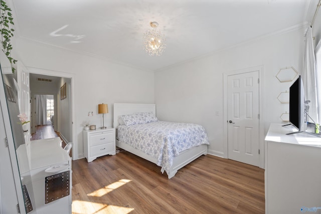 bedroom featuring a notable chandelier, crown molding, visible vents, and wood finished floors