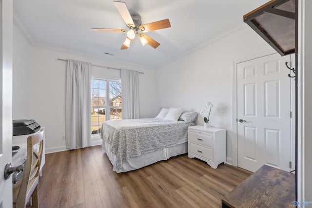 bedroom featuring visible vents, a ceiling fan, wood finished floors, crown molding, and baseboards