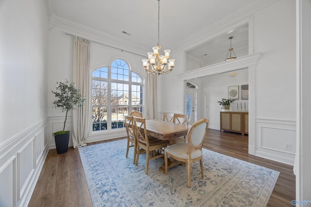 dining space with wood finished floors, a chandelier, crown molding, and a decorative wall