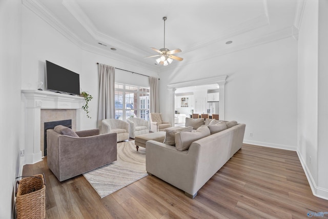 living area featuring a fireplace, a tray ceiling, wood finished floors, and ornamental molding