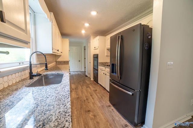 kitchen with white cabinetry, sink, light stone countertops, and stainless steel refrigerator with ice dispenser