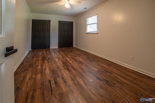 unfurnished bedroom with multiple closets, ornamental molding, ceiling fan, and dark hardwood / wood-style flooring