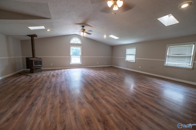 unfurnished living room featuring lofted ceiling, a wood stove, ceiling fan, dark wood-type flooring, and a textured ceiling