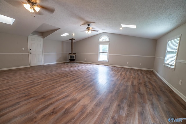 bonus room featuring dark hardwood / wood-style flooring, ceiling fan, vaulted ceiling with skylight, and a wood stove