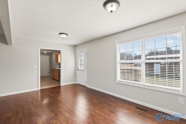 empty room featuring dark wood-style floors, a textured ceiling, visible vents, and baseboards