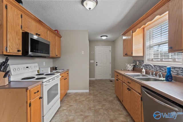 kitchen featuring baseboards, brown cabinetry, stainless steel appliances, light countertops, and a sink