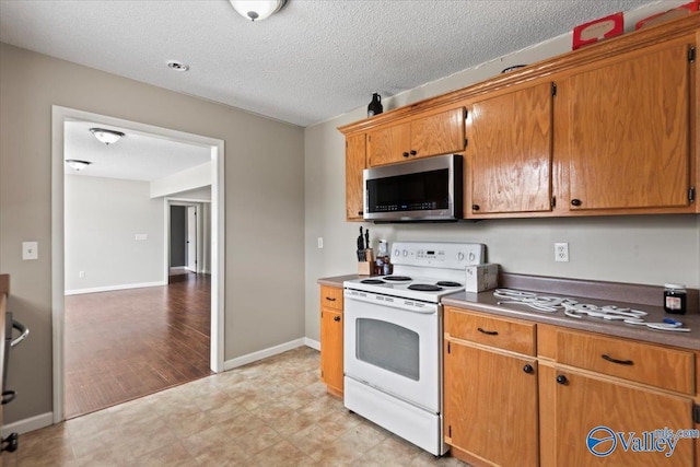 kitchen with white electric stove, a textured ceiling, baseboards, brown cabinets, and stainless steel microwave