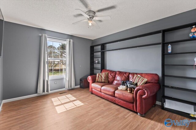 living area featuring a textured ceiling, wood finished floors, a ceiling fan, and baseboards