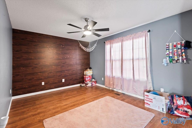 interior space with wooden walls, baseboards, an accent wall, wood finished floors, and a textured ceiling