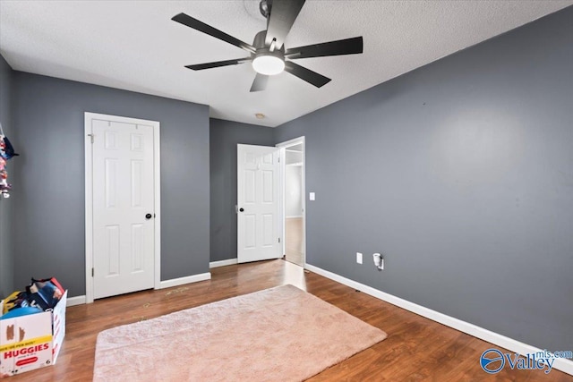 unfurnished bedroom with ceiling fan, a textured ceiling, baseboards, and wood finished floors