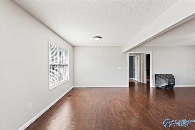 empty room featuring a textured ceiling, dark wood-style flooring, and baseboards