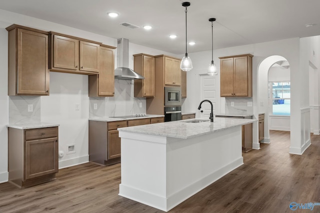 kitchen with a kitchen island with sink, wall chimney exhaust hood, stainless steel appliances, and dark hardwood / wood-style flooring