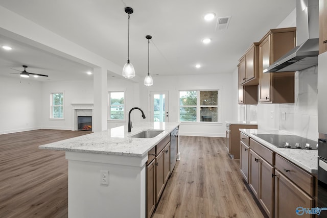 kitchen with light wood-type flooring, a kitchen island with sink, wall chimney exhaust hood, sink, and black electric stovetop