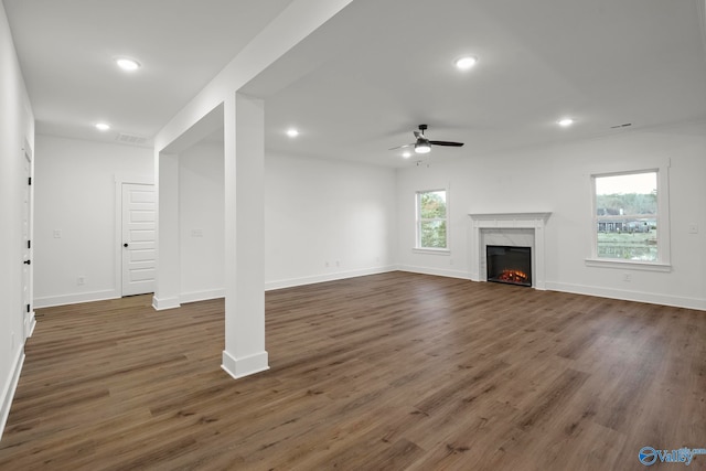 unfurnished living room featuring ceiling fan, a fireplace, dark hardwood / wood-style flooring, and a wealth of natural light