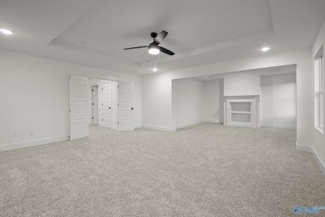 interior space with light carpet, ceiling fan, and a tray ceiling