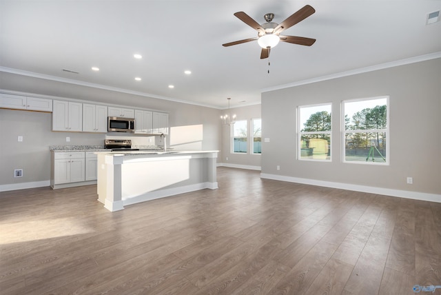 kitchen with pendant lighting, white cabinetry, stainless steel appliances, ornamental molding, and a center island with sink